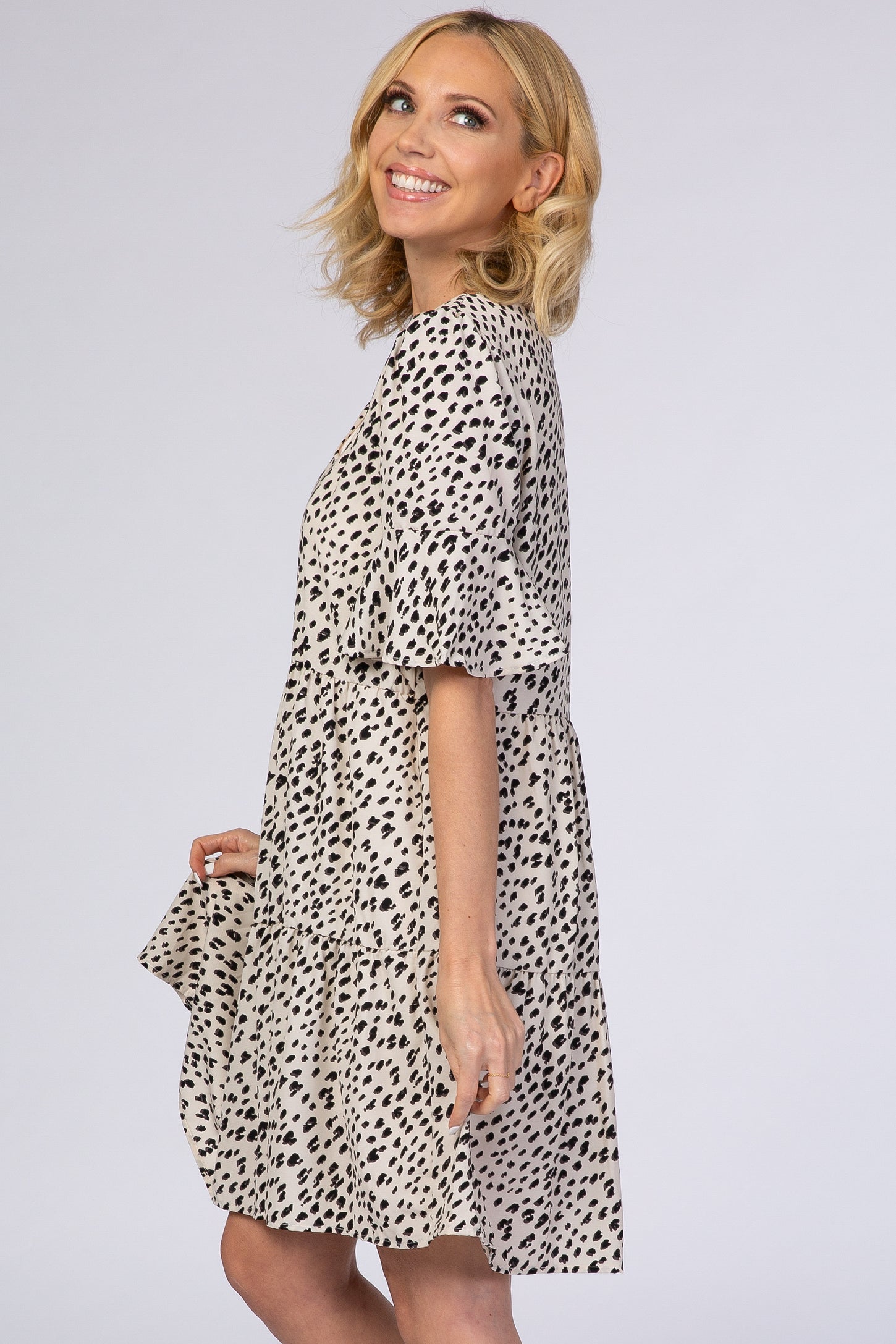woman wearing a short, flared beige dress with black spots and bell sleeves, smiling and facing to the side