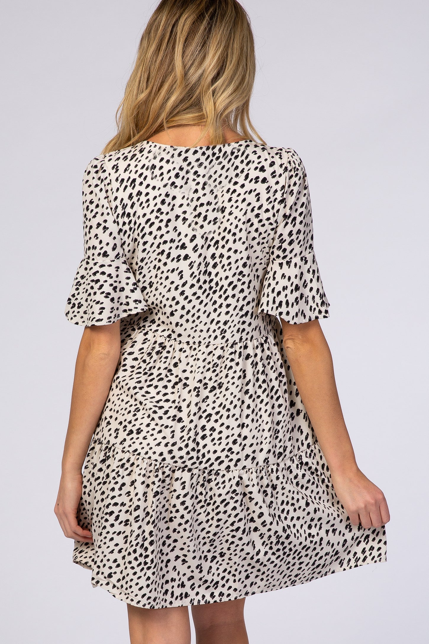 woman wearing a spotted maternity dress with ruffle sleeves and a tiered skirt, showing the back view