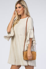 woman wearing a beige bohemian style dress with bell sleeves and fringe details, holding a woven crossbody bag