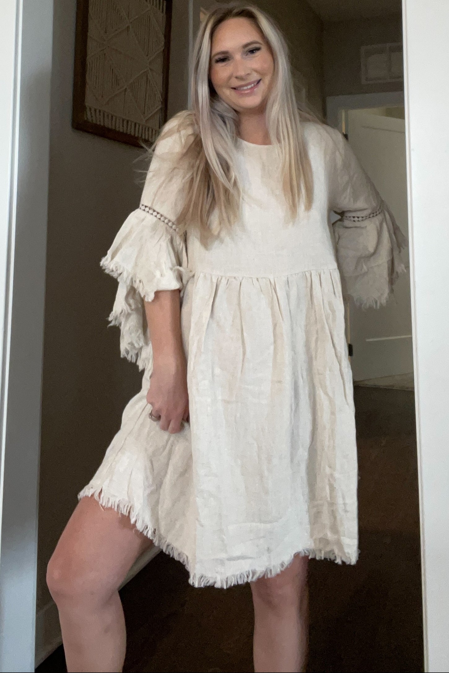 woman wearing a light beige loose-fitting dress with bell sleeves and fringe detailing