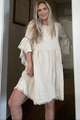 woman wearing a light beige loose-fitting dress with bell sleeves and fringe detailing