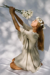 woman wearing a light beige flowy dress with bell sleeves, holding flowers and wearing a flower crown