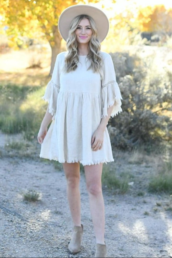 woman wearing a beige short sleeve dress with fringe details and a wide-brimmed hat in a outdoor setting