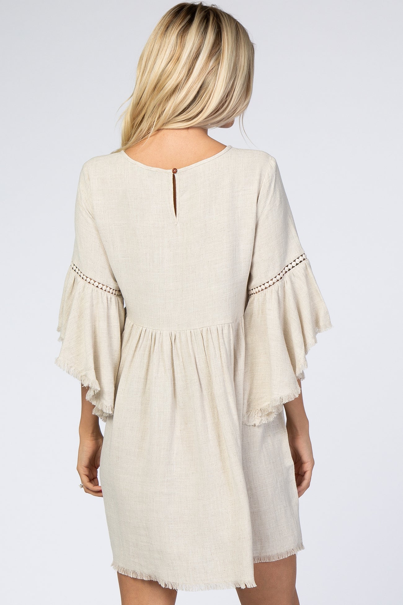woman wearing a beige short sleeve dress with fringe and detailed stitching, showing the back view