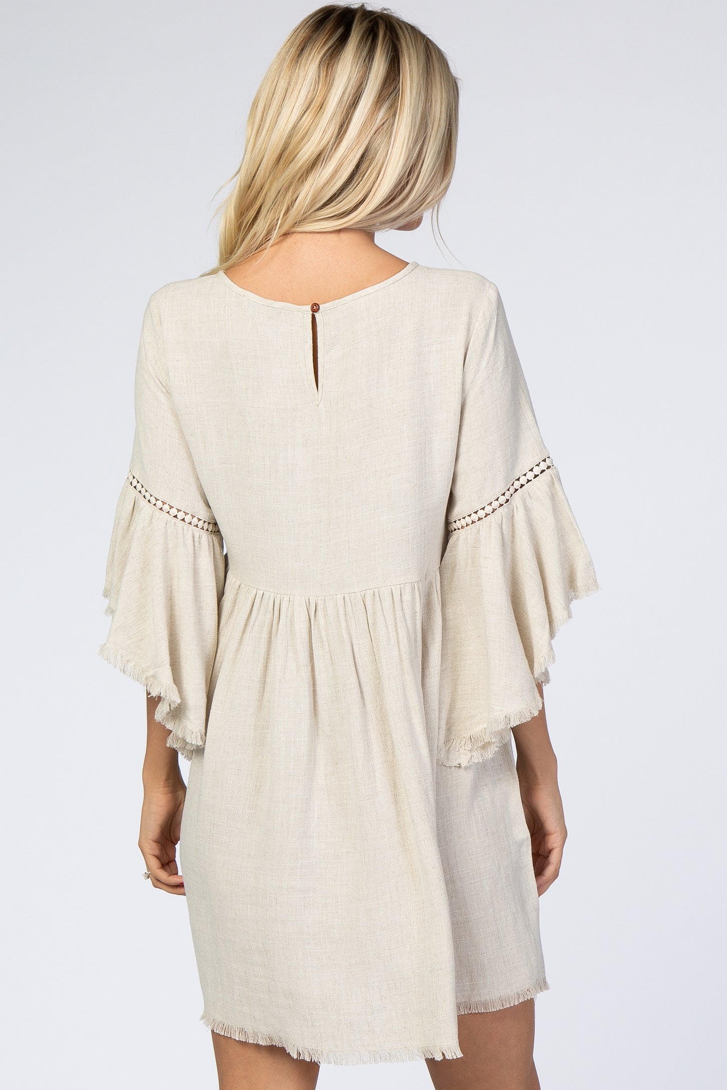 woman wearing a beige short sleeve dress with fringe and detailed stitching, showing the back view