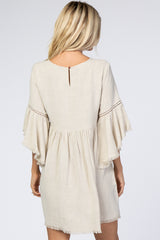 woman wearing a beige short sleeve dress with fringe and detailed stitching, showing the back view