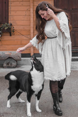 woman wearing a light gray fringed dress and black rain boots, petting a black and white dog outdoors
