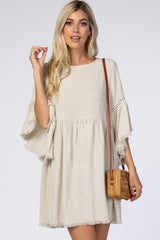 Woman wearing a beige linen babydoll dress with fringe bell sleeves and a woven straw crossbody bag