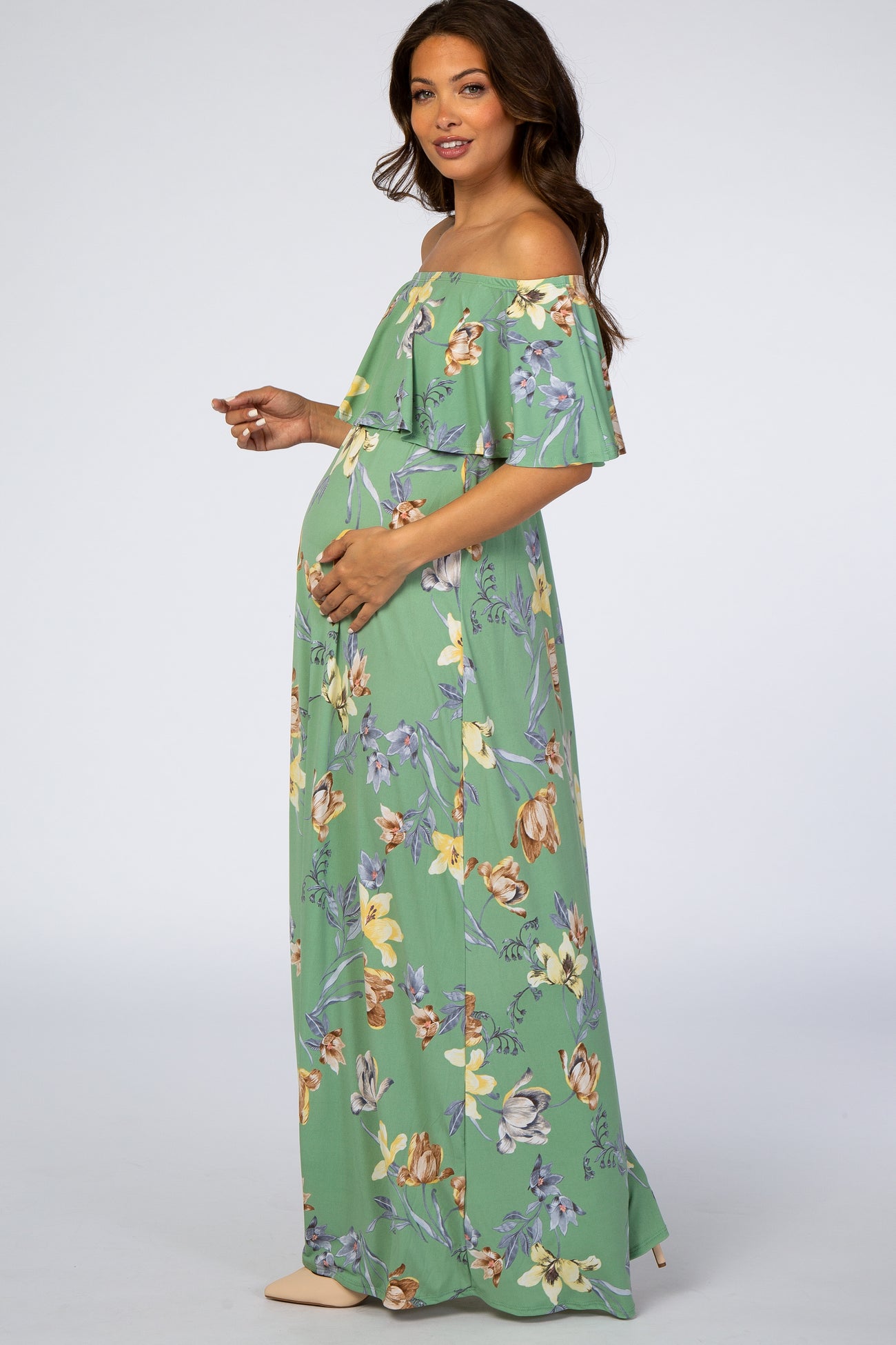 woman wearing a floral off-the-shoulder maternity maxi dress and gently holding her baby bump