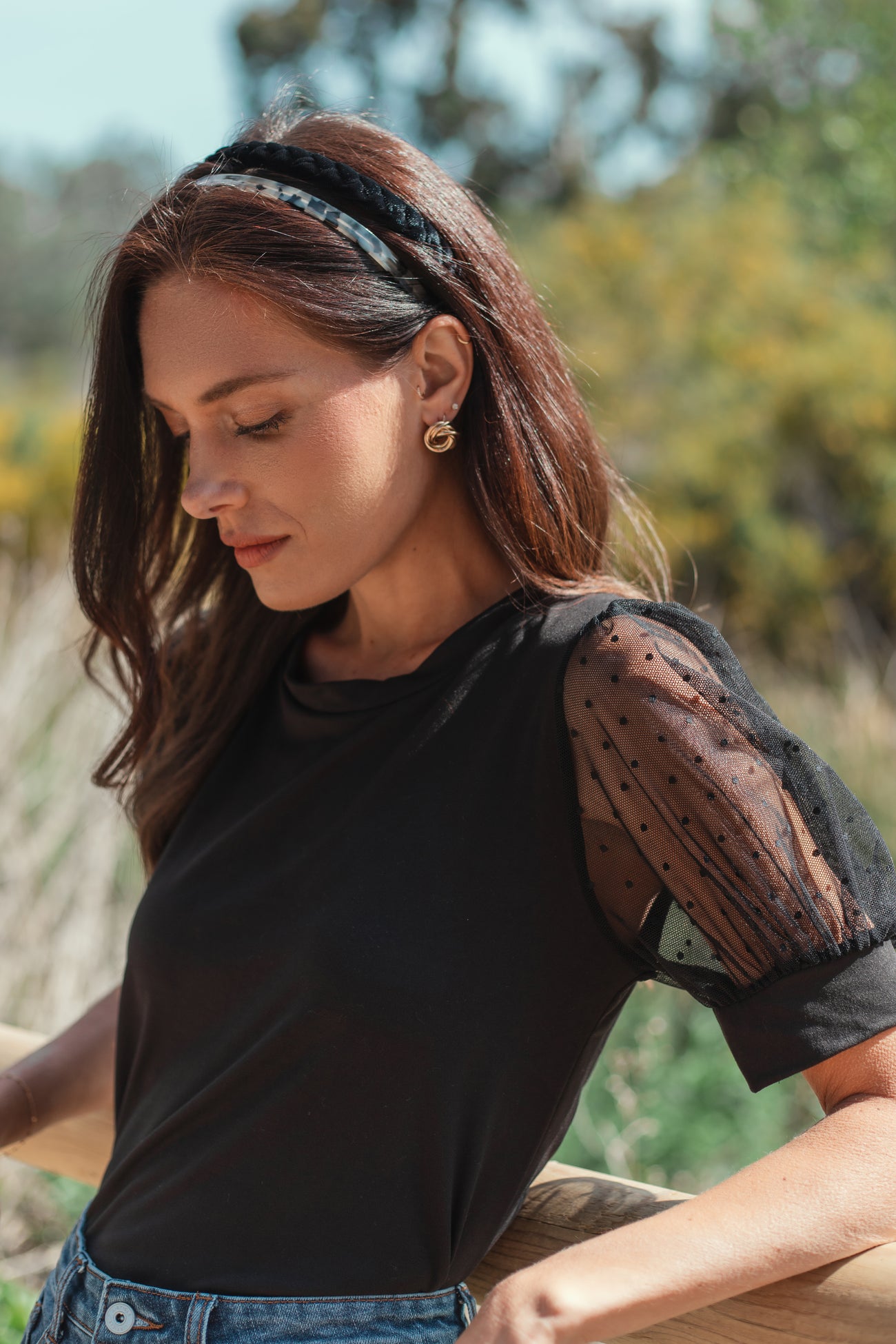 woman wearing a black t-shirt with sheer polka dot puff sleeves and a black headband outdoors