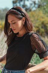woman wearing a black t-shirt with sheer polka dot puff sleeves and a black headband outdoors