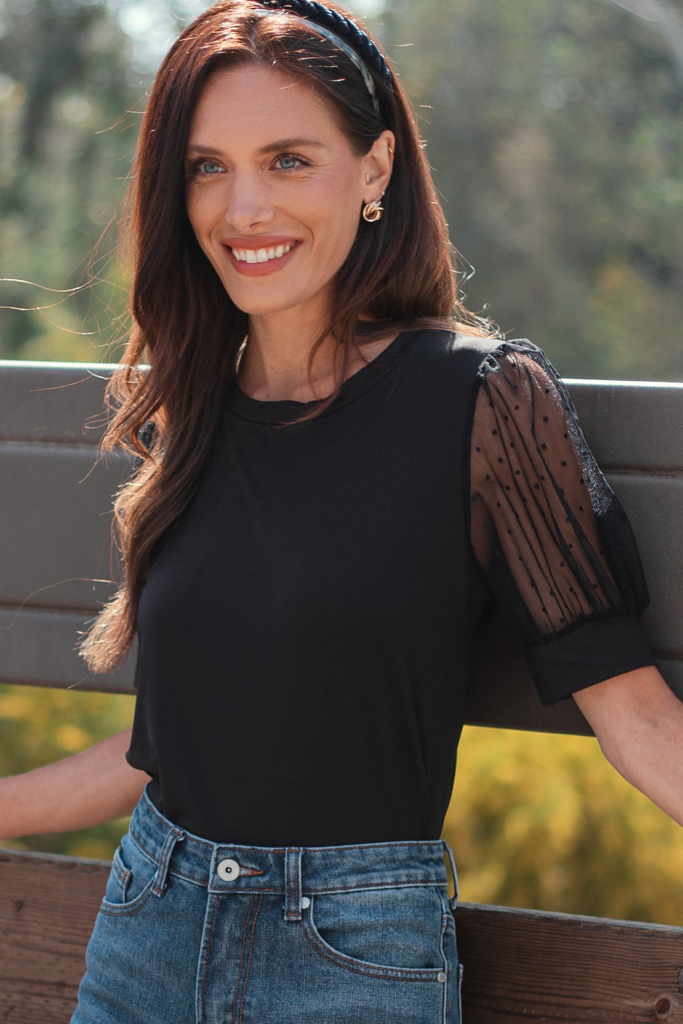 woman wearing a black top with sheer puff sleeves and denim high-waisted shorts, smiling outdoors
