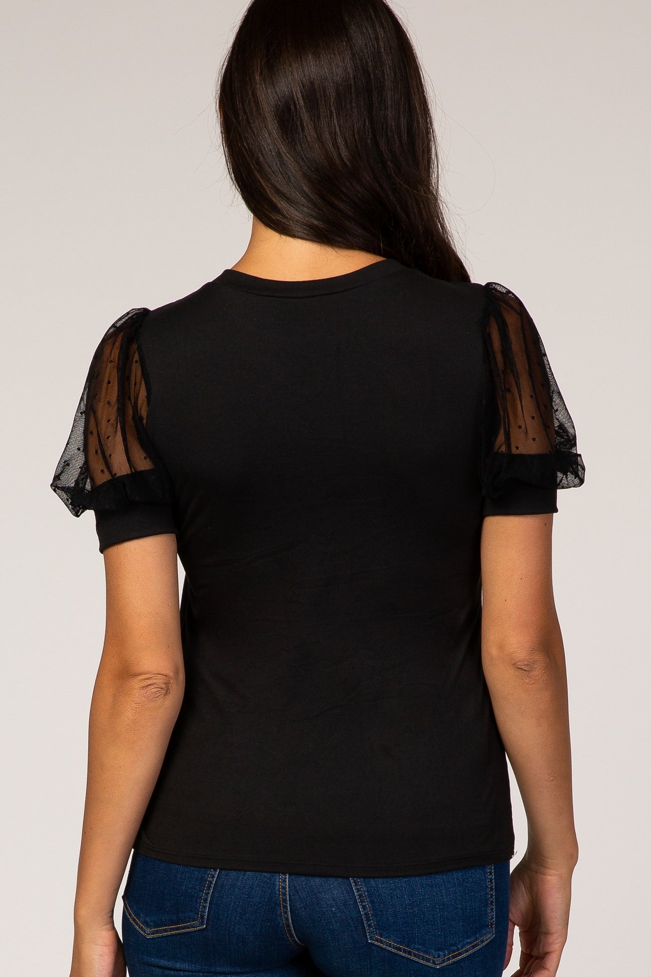 black t-shirt with sheer polka dot puff sleeves, worn by a woman facing away, styled with blue jeans