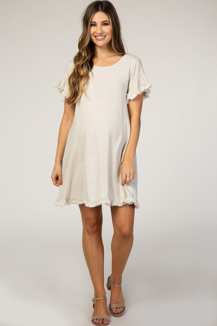 woman wearing a beige maternity dress with ruffle sleeves and a flared hem, showing a baby bump