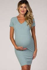 woman wearing a light blue short sleeve maternity dress, gently cradling her baby bump