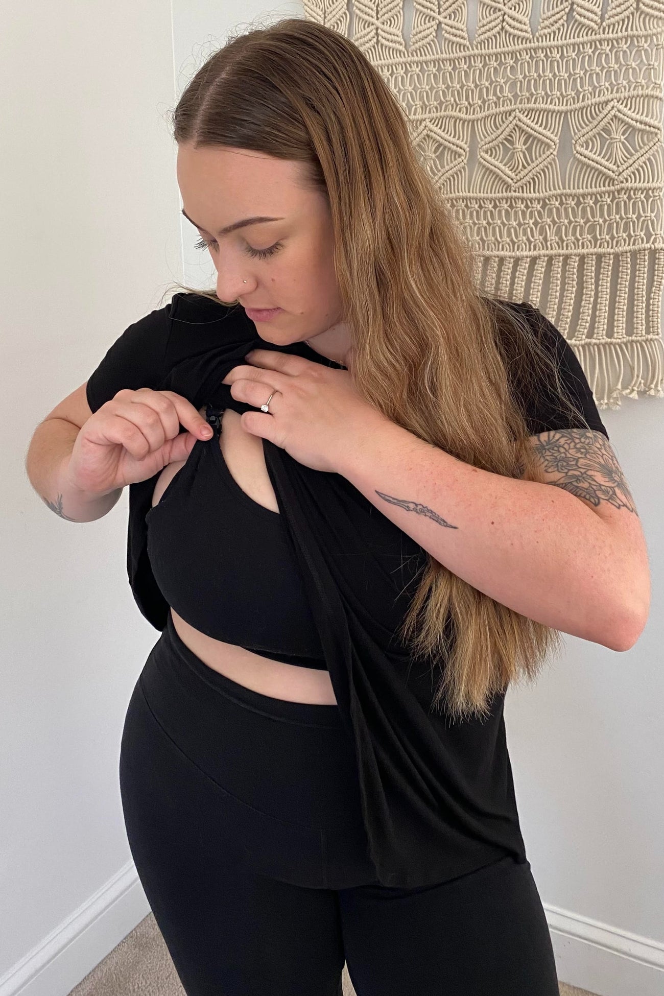 woman wearing a black nursing top, adjusting the fabric for easy access, paired with black leggings