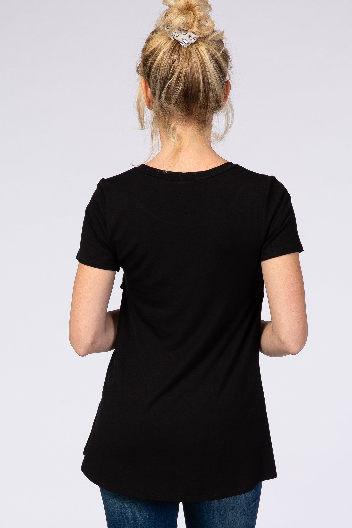 woman wearing a black short sleeve top from the back, styled with jeans and hair in a bun