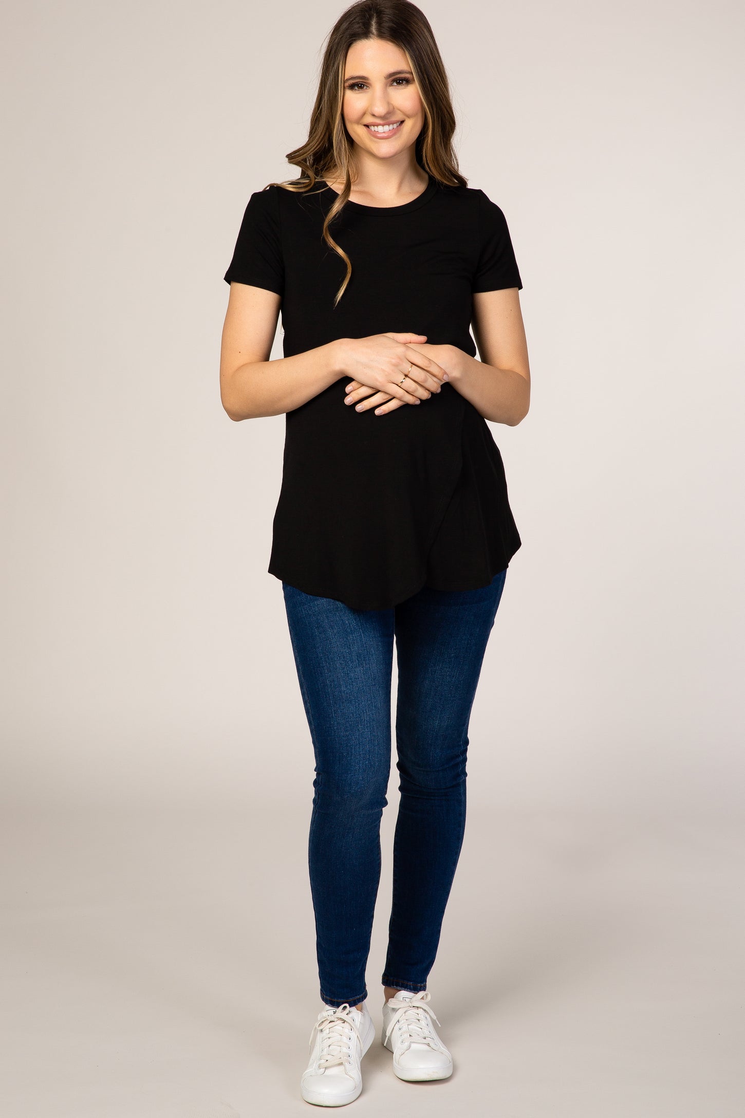woman wearing a black short sleeve maternity top and showcasing her baby bump with blue skinny jeans