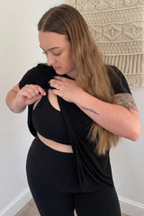 woman wearing a black nursing top, adjusting the fabric for easy access, paired with black leggings
