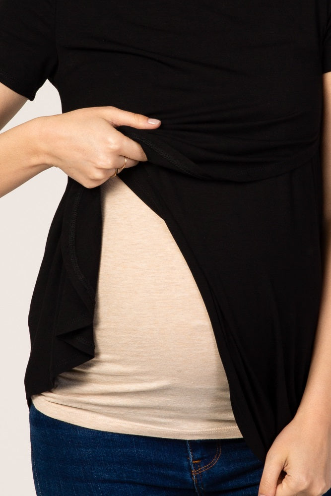 woman wearing a black maternity top, lifting it to reveal her baby bump with a beige undershirt beneath