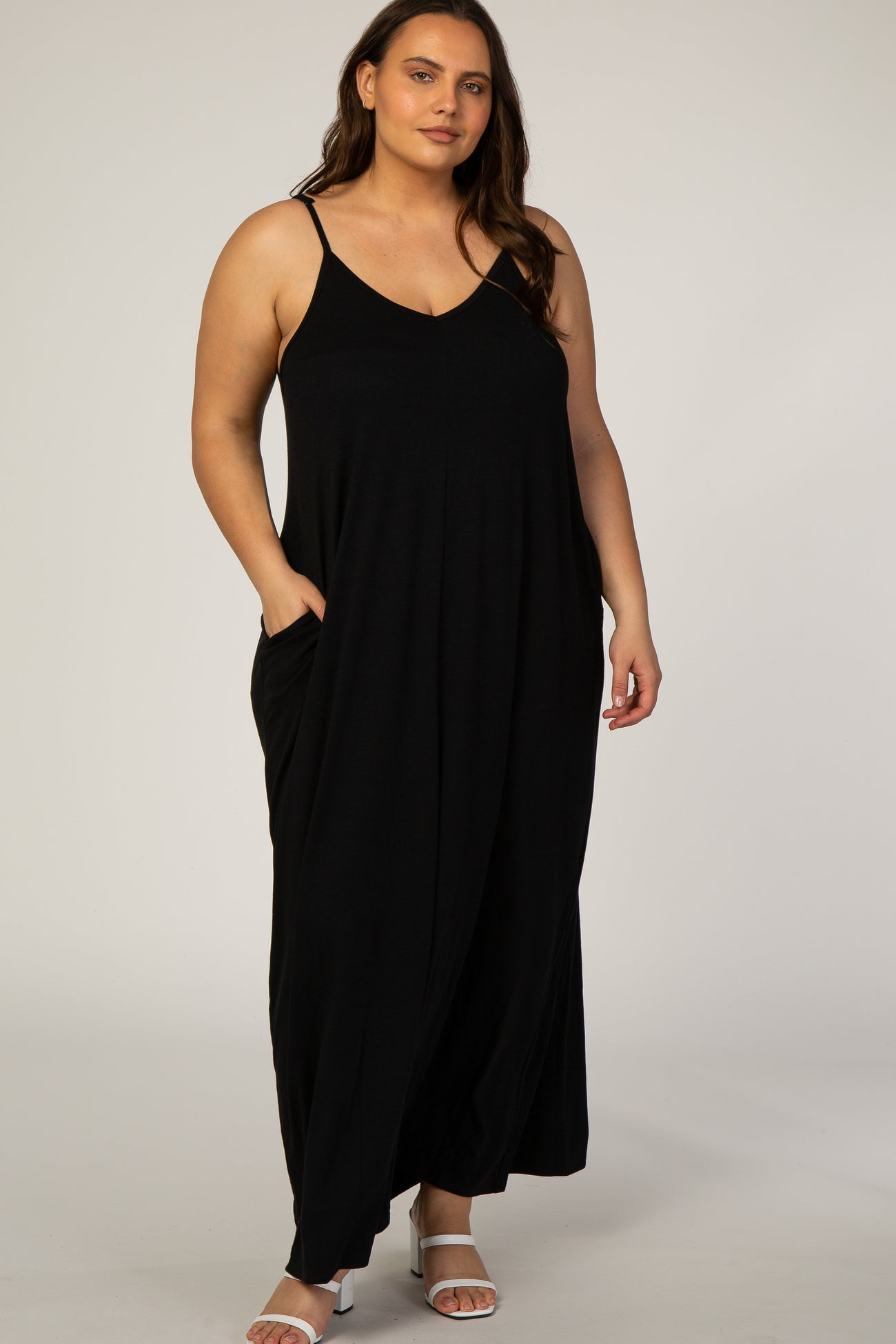woman wearing a plus size black sleeveless maxi dress with pockets and white strappy sandals