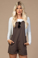 woman wearing a brown overall romper with pockets and a white long sleeve shirt, accessorized with sunglasses