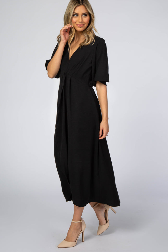 woman wearing a black short sleeve maxi dress with a tie waist and a v-neckline, standing in profile