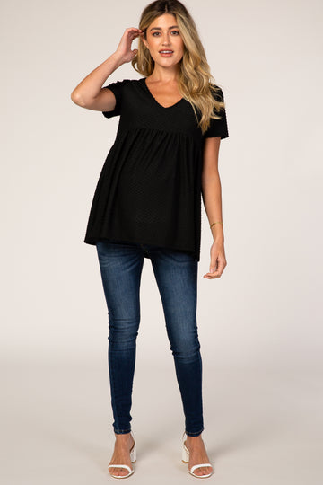 woman wearing a black short sleeve maternity top with a v-neck and flowing bottom, paired with blue skinny jeans