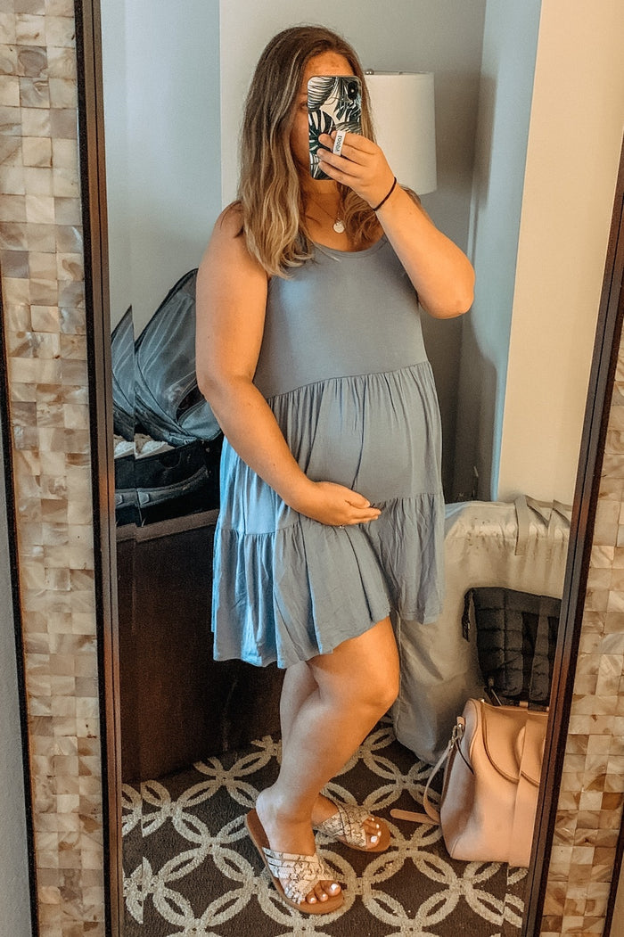 woman wearing a light blue maternity dress with a tiered skirt and holding her baby bump in front of a mirror