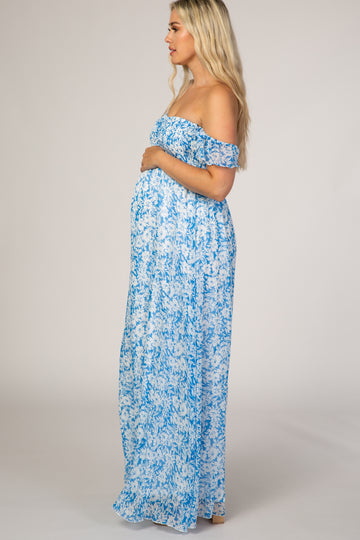 woman wearing a blue off-the-shoulder maternity maxi dress and cradling her baby bump