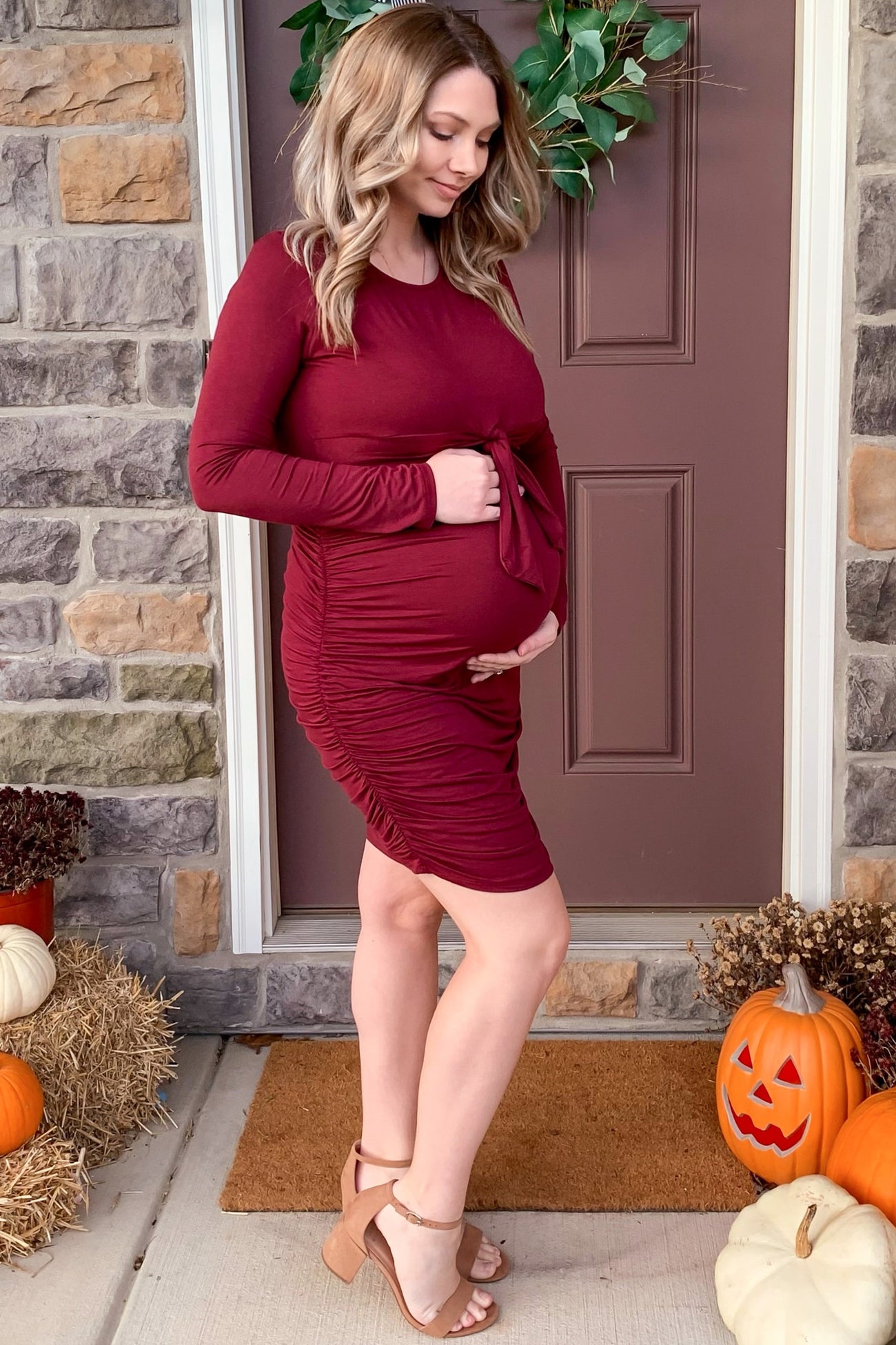 woman wearing a burgundy long sleeve maternity dress with ruching and a tied detail, showing her baby bump