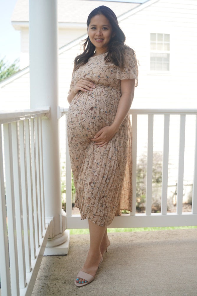 woman wearing a floral beige maternity dress with flutter sleeves and holding her baby bump