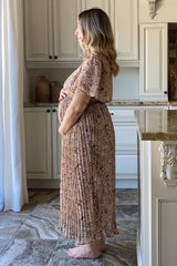 woman wearing a floral pleated maxi maternity dress and holding her baby bump