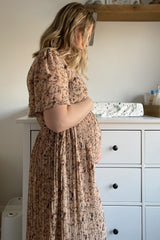 woman wearing a floral maternity dress and holding her baby bump, styled in a side profile