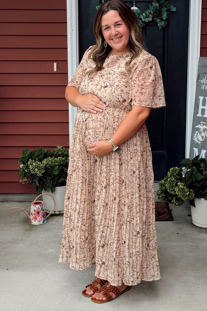 woman wearing a blush floral pleated maternity maxi dress and holding her baby bump