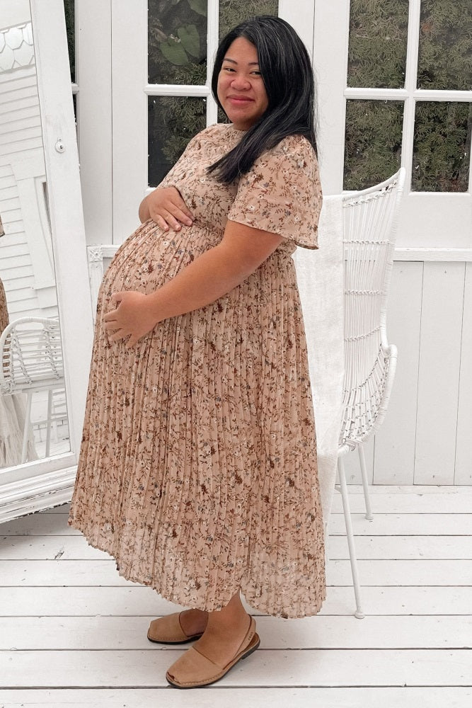 woman wearing a floral pleated maternity dress with a visible baby bump and posing in a bright setting