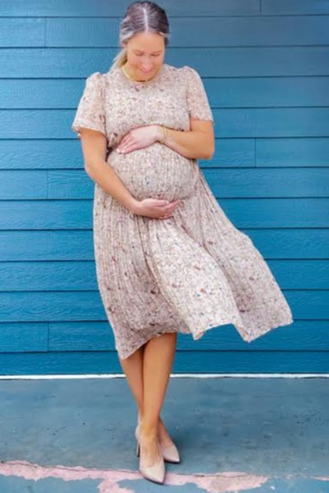 pregnant woman in floral maternity dress holding her baby bump against a blue wooden wall