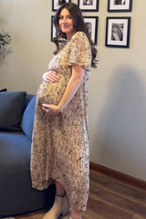 woman wearing a floral print maternity dress with a tiered skirt, holding her baby bump while standing by a sofa