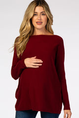woman wearing a burgundy maternity sweater with a boat neckline and holding her baby bump