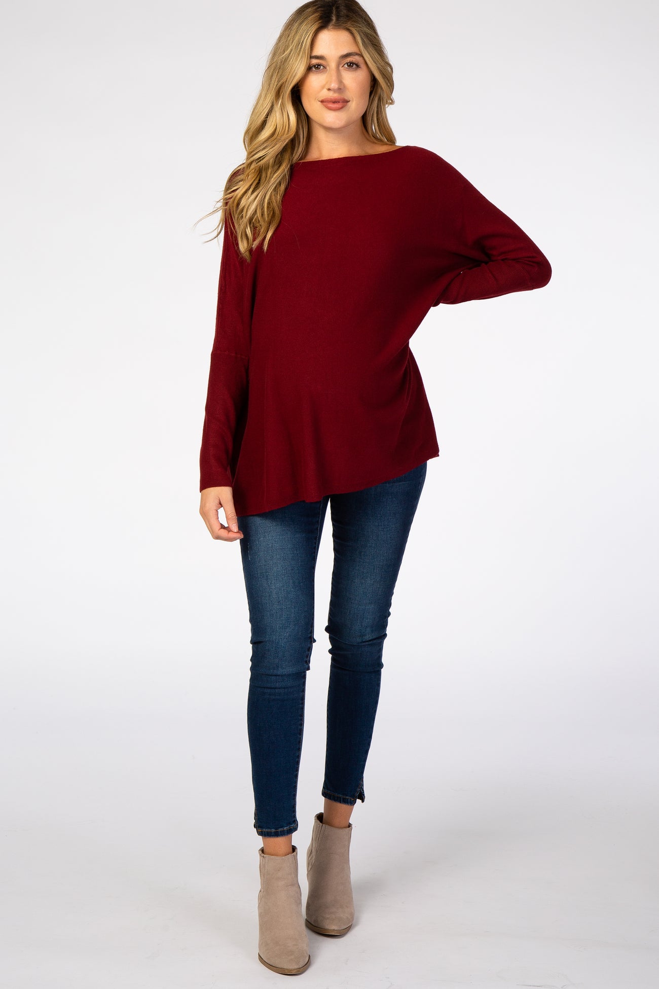 woman wearing a burgundy long sleeve maternity top with blue skinny jeans and tan ankle boots