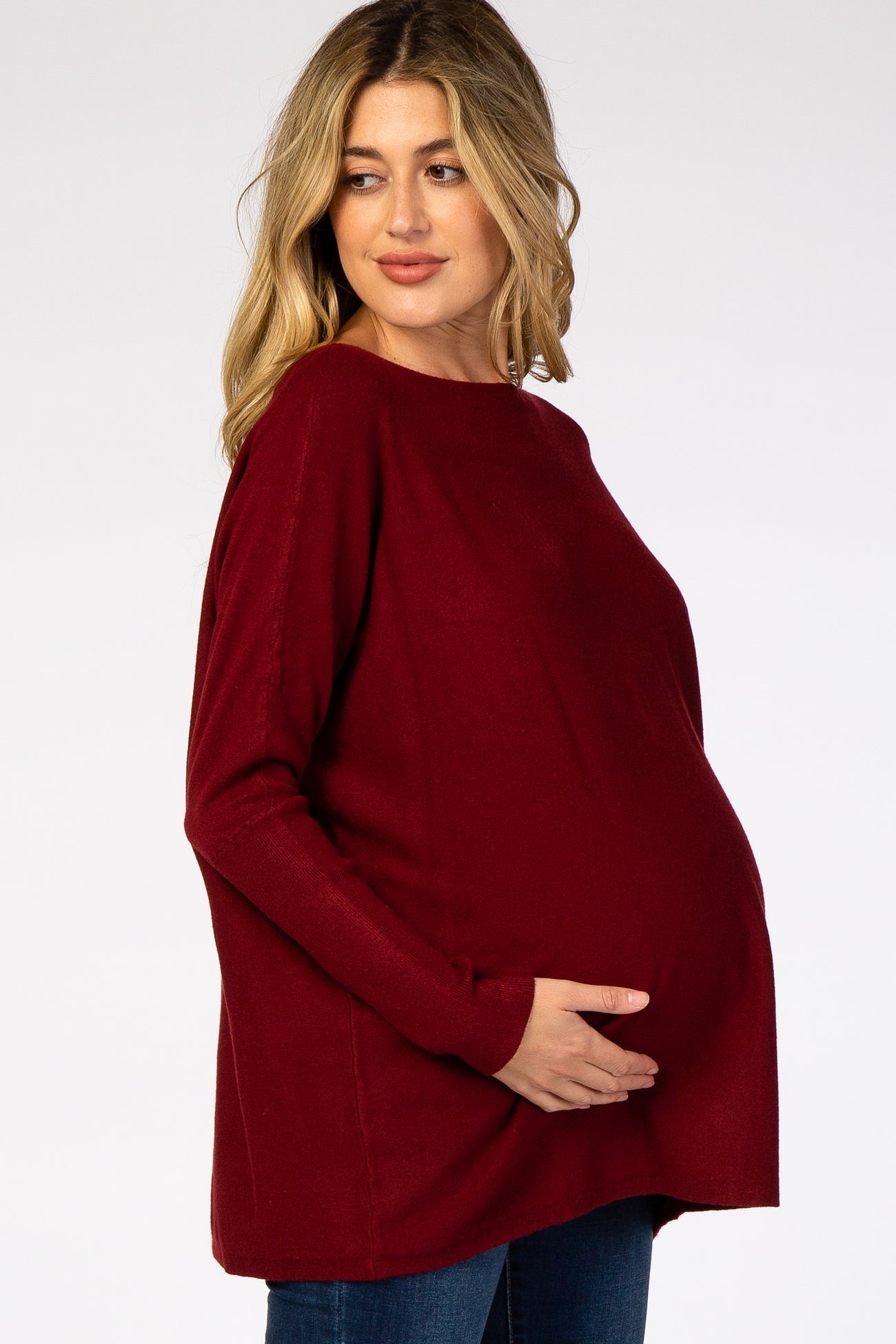 woman wearing a burgundy oversized maternity sweater and holding her baby bump