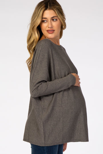 pregnant woman wearing a grey oversized maternity sweater and blue jeans against a white background