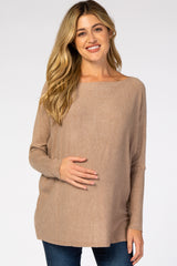 smiling pregnant woman wearing a tan boat neck maternity sweater and blue jeans
