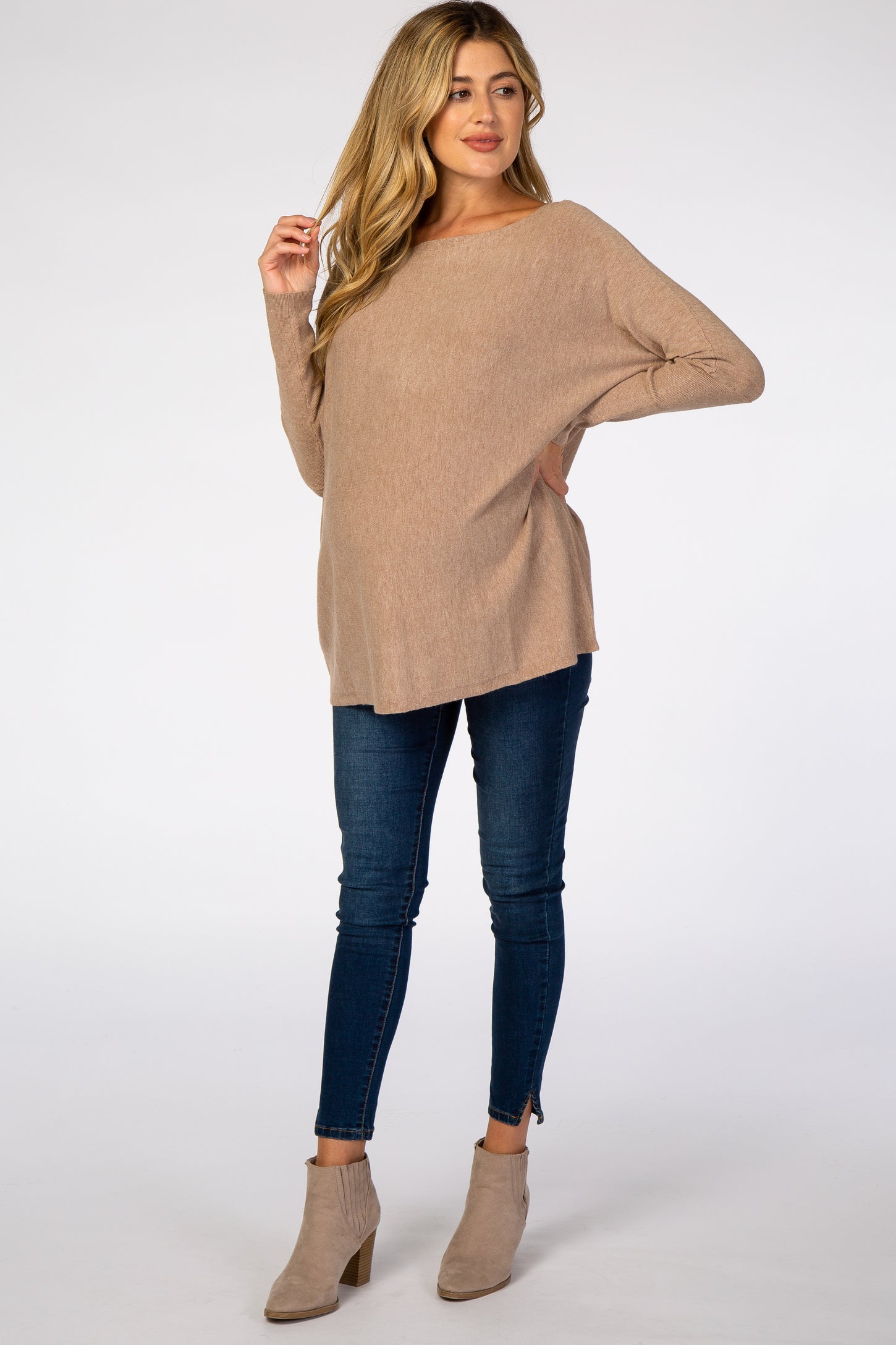 woman wearing a beige maternity sweater with a loose fit and a visible baby bump, paired with dark skinny jeans and ankle boots