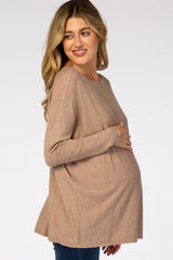 woman wearing a beige long sleeve maternity top and holding her baby bump