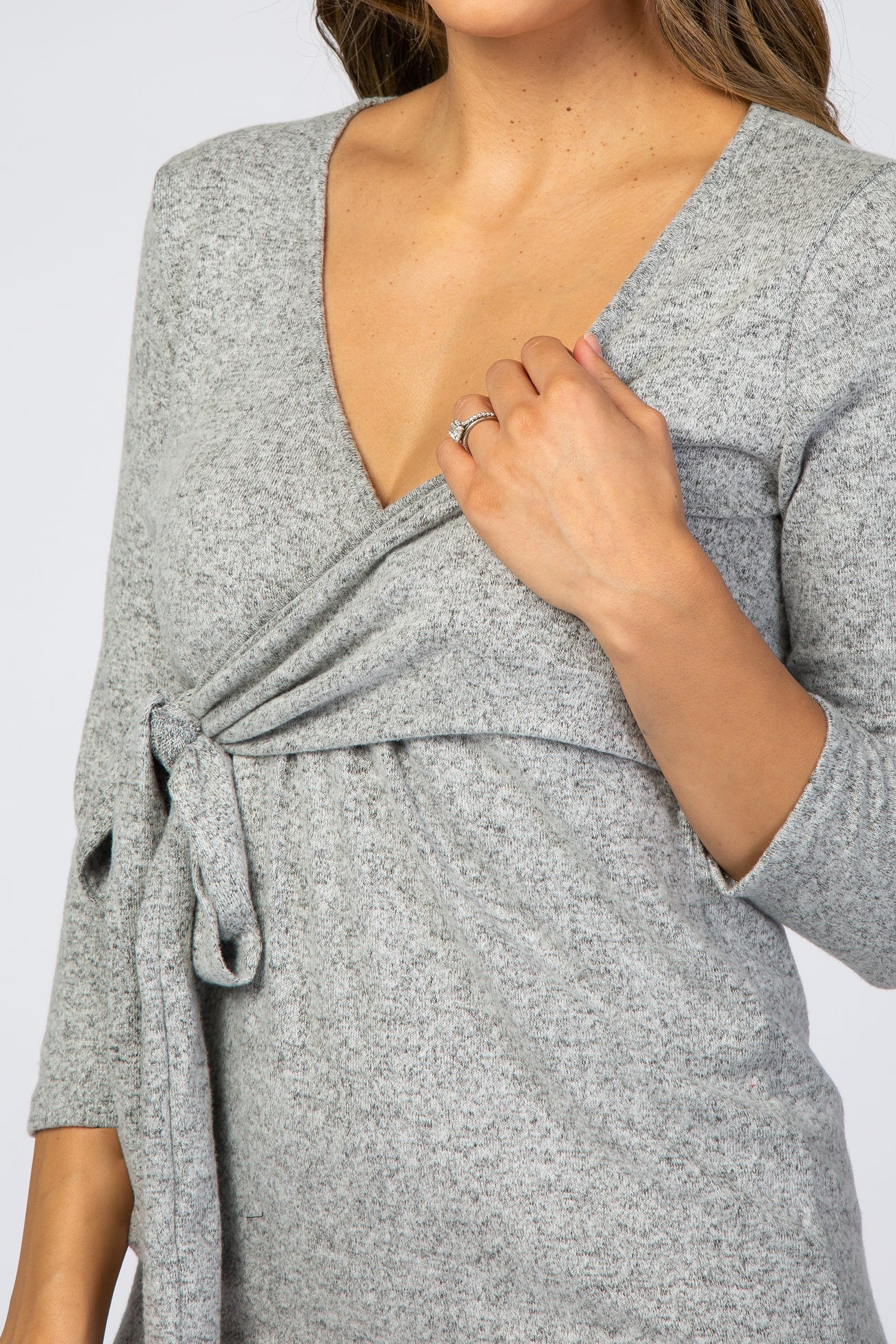 woman wearing a gray long sleeve top with a v-neck and tie detail at the waist