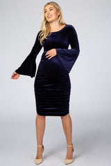 Pregnant woman wearing a navy blue velvet maternity dress with bell sleeves and ruched detailing