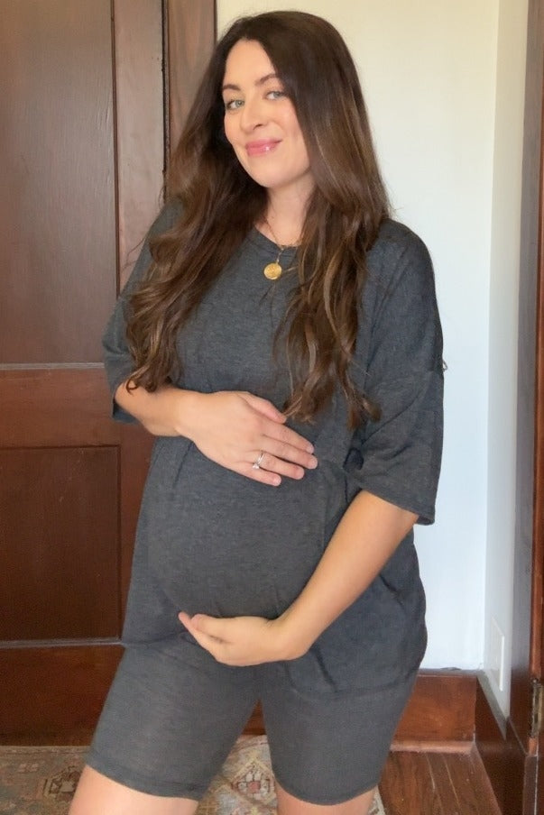 Pregnant woman in charcoal grey maternity lounge set smiling and holding her baby bump
