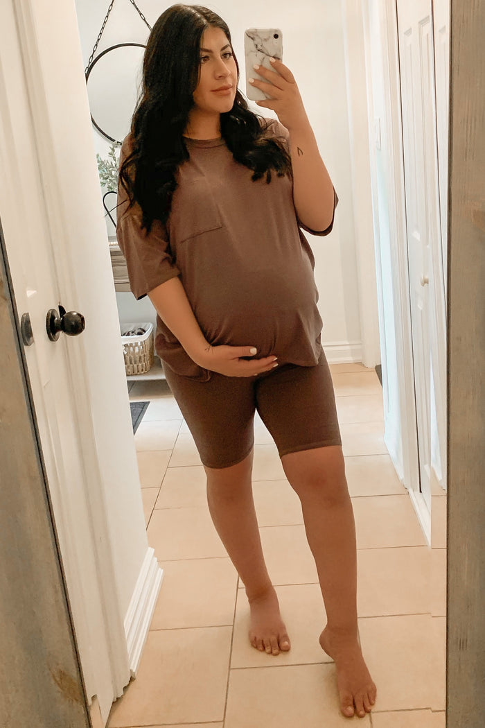 woman wearing a brown maternity active set with a short sleeve top and bike shorts, showing her baby bump