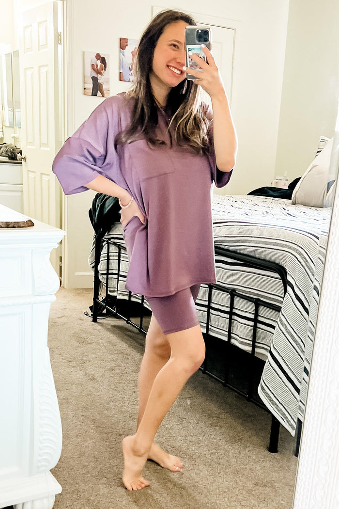 woman wearing a loose-fitting mauve oversized top with a pocket and matching bike shorts, posing in a mirror